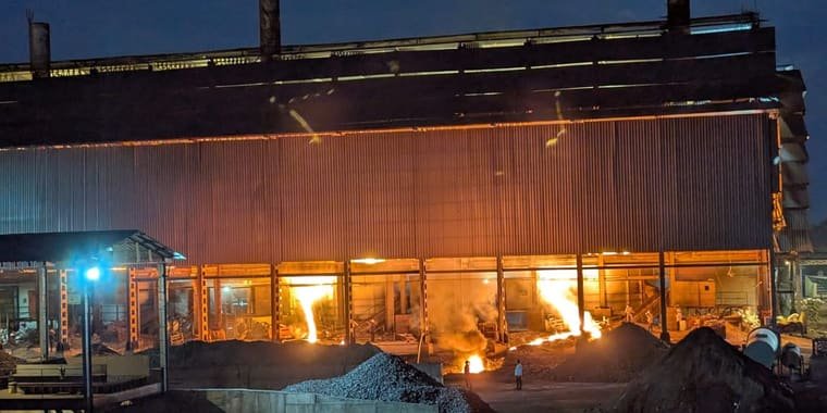 Molten alloy tapped from the furnaces at dusk, seen through the open side of the furnace building