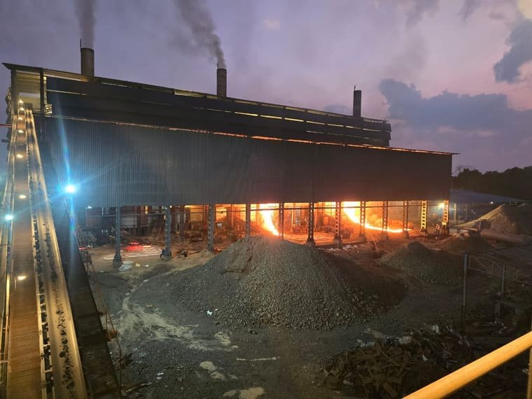 The works at dusk: the charging conveyor climbing to the furnace building, stacks smoking, the tap glow running the length of the bays