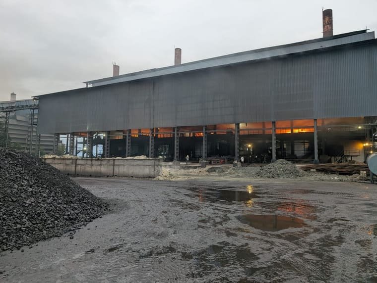 Manganese ore stockpiled in the yard in front of the furnace shed, with the tap glow showing between the columns