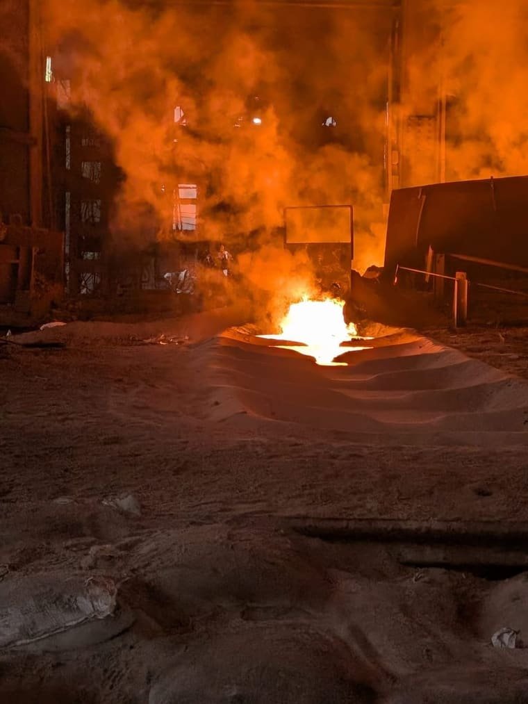 Molten alloy running white from the tap hole down a sand runner into the casting bed